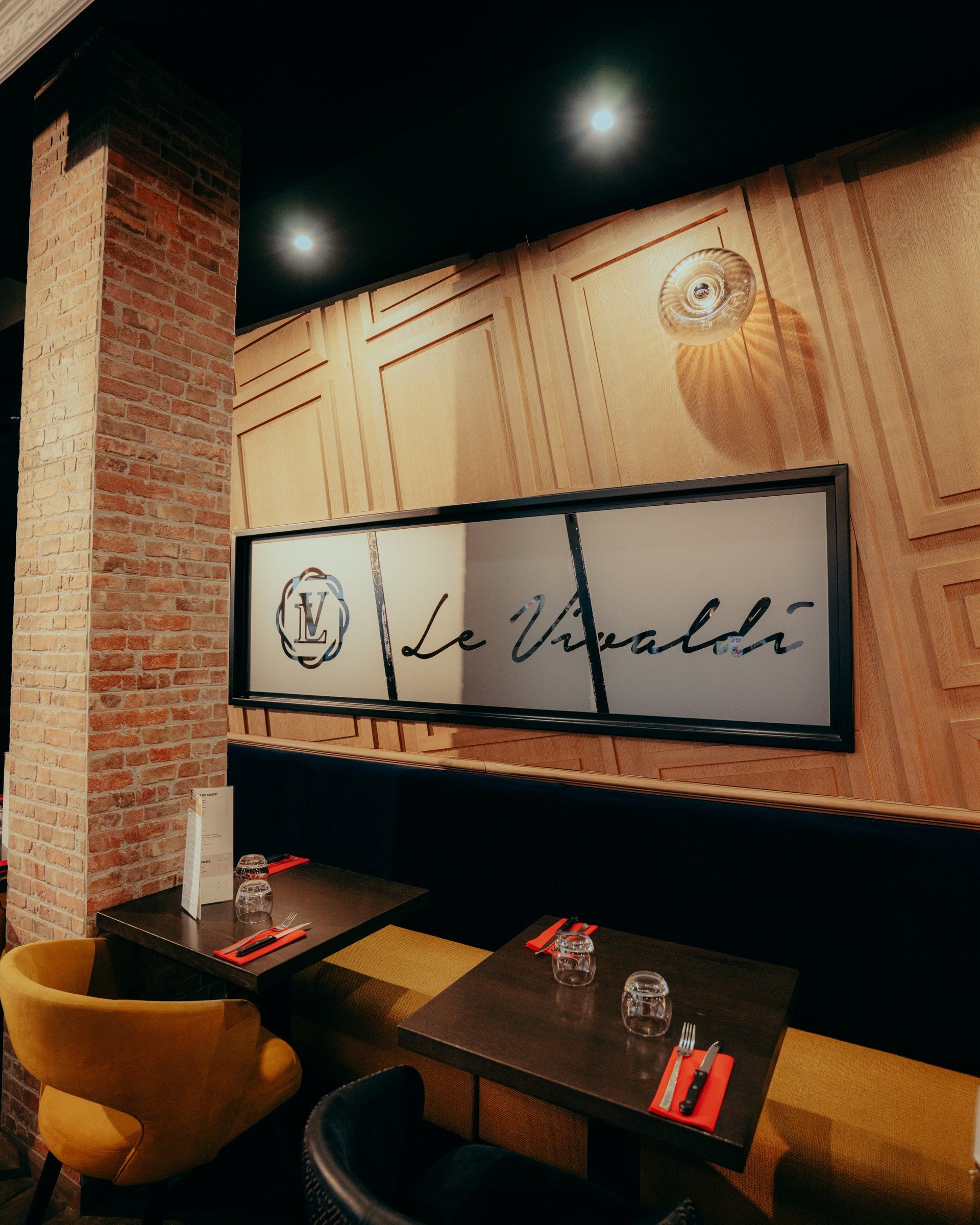 Banquettes le long du mur en bois, enseigne Le Vivaldi et fauteuils moutarde